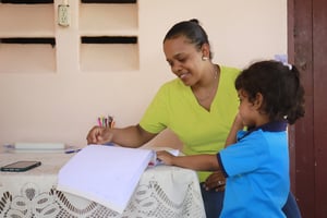 A woman in a yellow shirt helps a small girl in a blue shirt looking through a book in the Dominican Republic