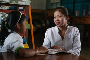 A teacher talks with a girl as they look at a book together