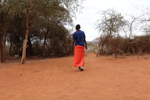 A young woman walks away from camera along a dusty path among scrup brush