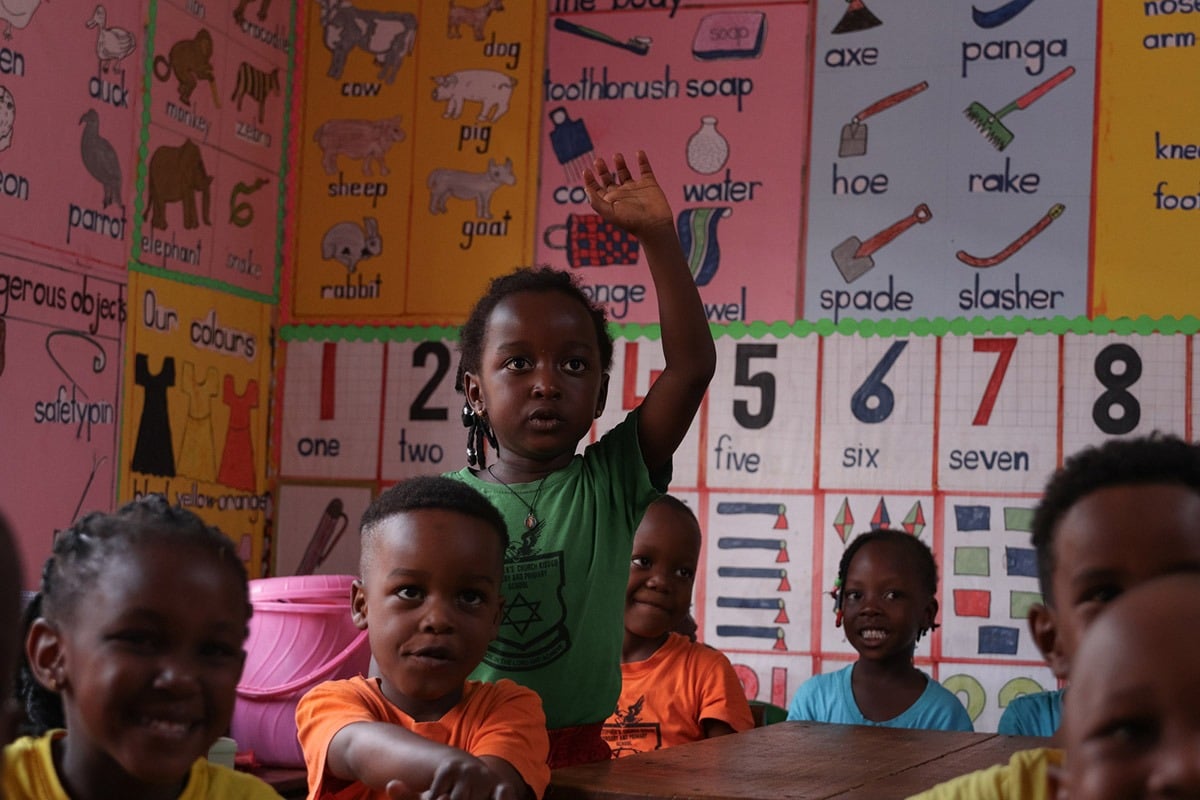 A little girl raising her hand in a  classroom in Uganda