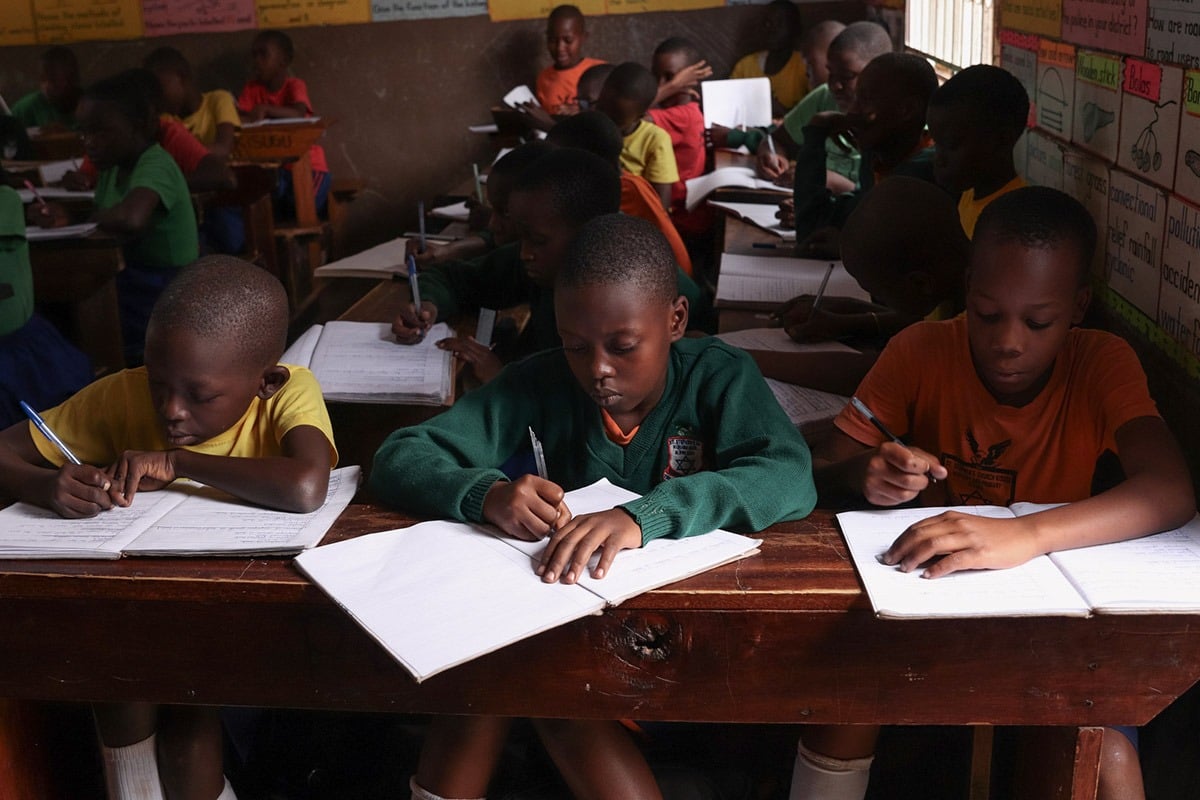 Children writing in notebooks in a classroom in Uganda