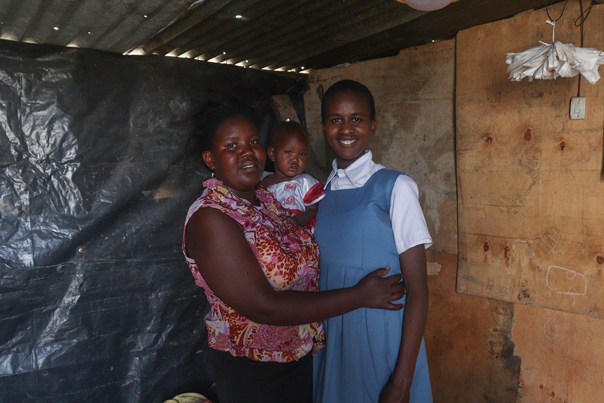 A mother with an infant and teenage daughter inside a small house in Kenya