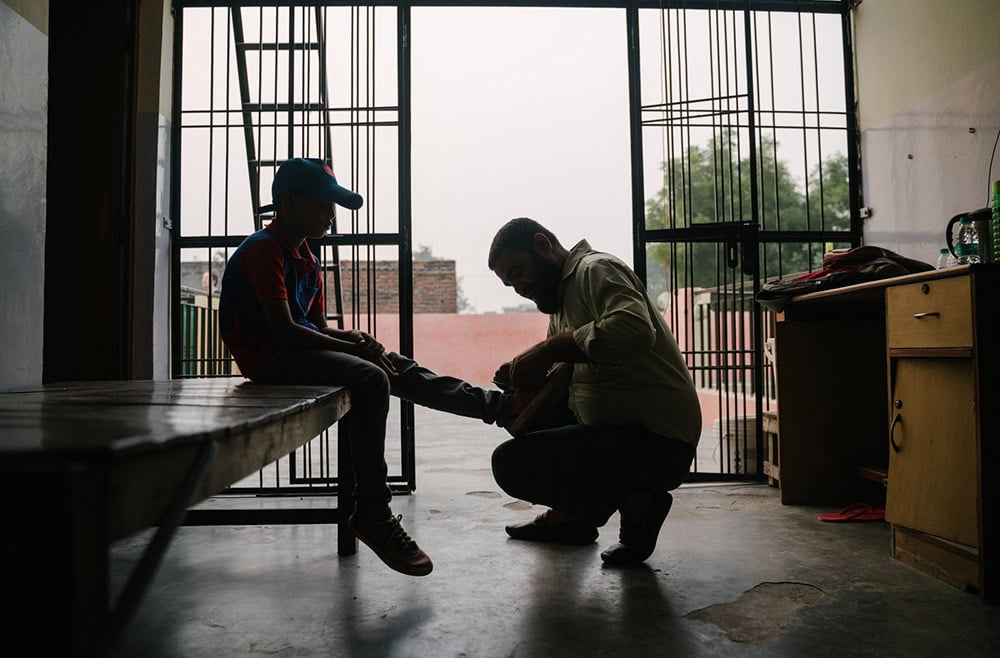 Silhouetted against the light, a Child Champion helps a boy tie his shoe. 