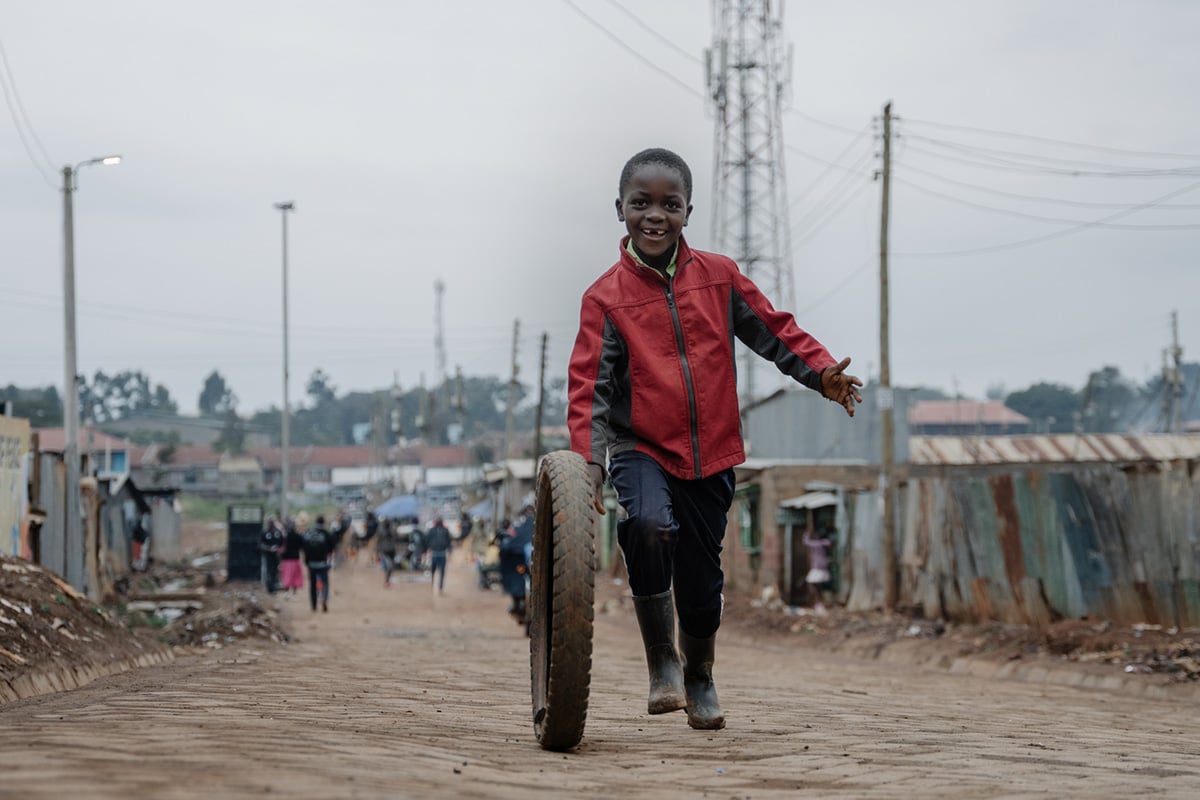 Smiling boy running through a slum pushing a wheel as a toy