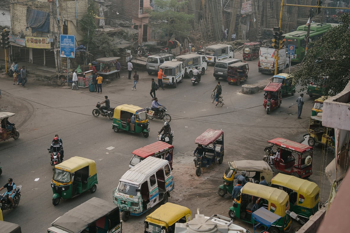 An overhead view of an intersection in India crowded with yellow and green auto-rickshaws