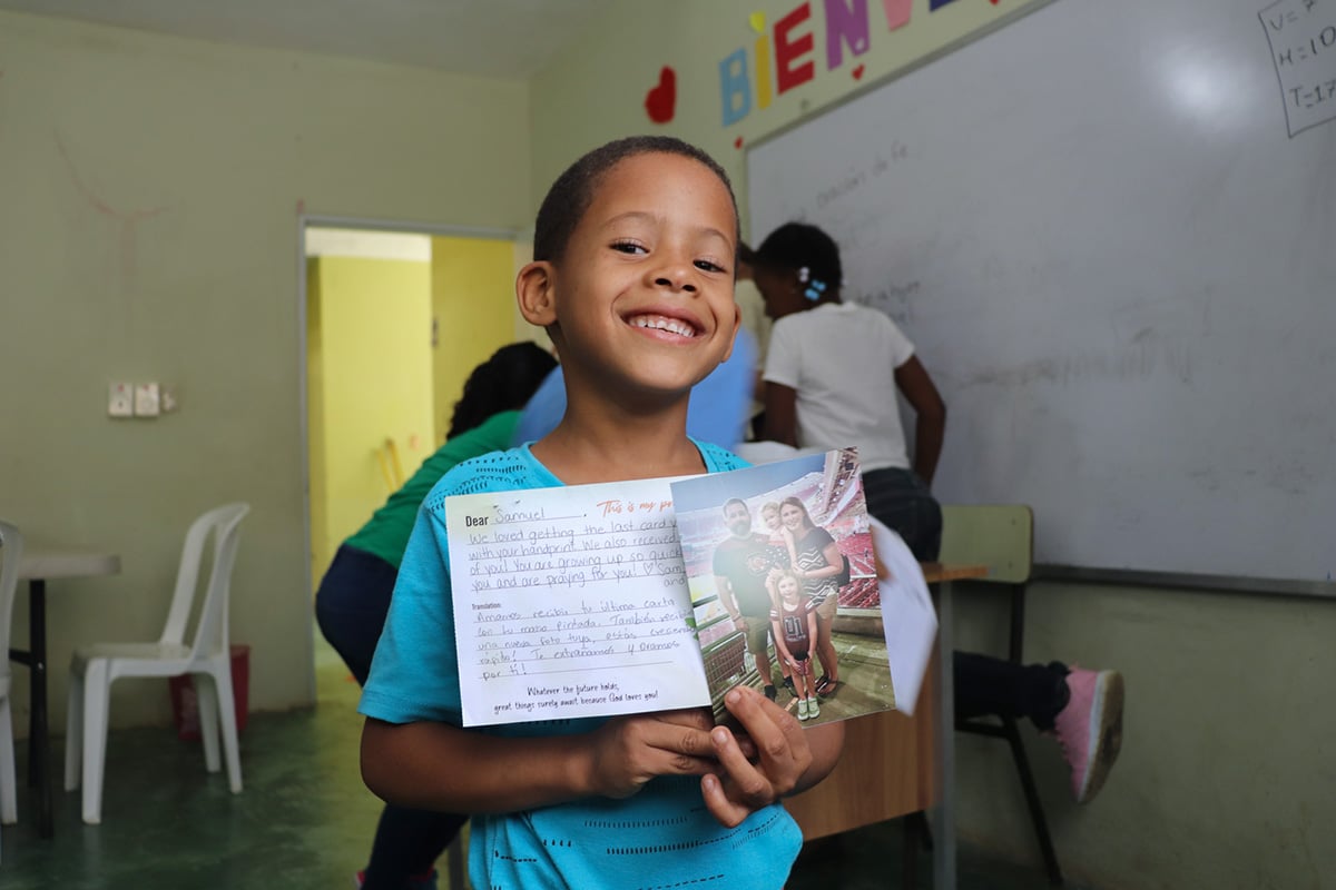 A boy holding a photo and letter from his sponsor